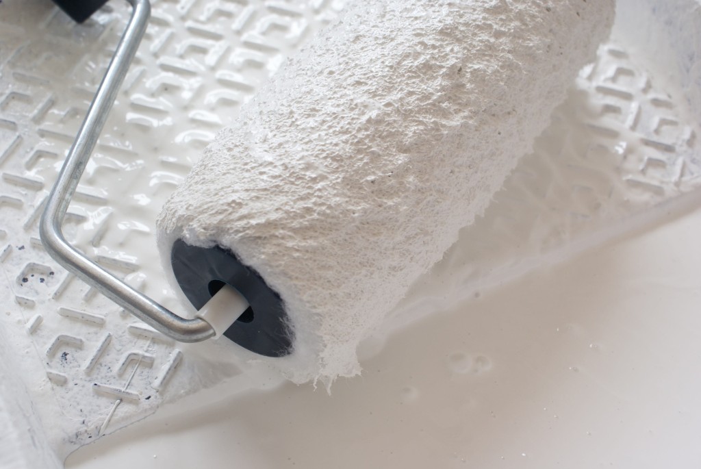 Paint roller in white paint ready for use.