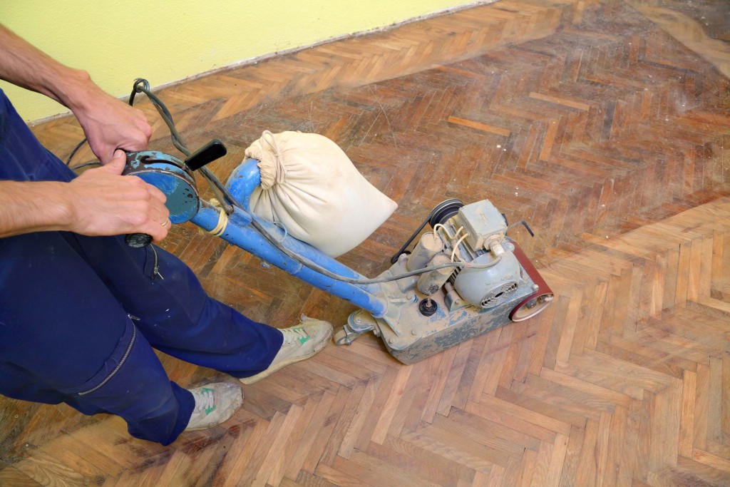 Worker polishing old parquet floor with grinding machine
