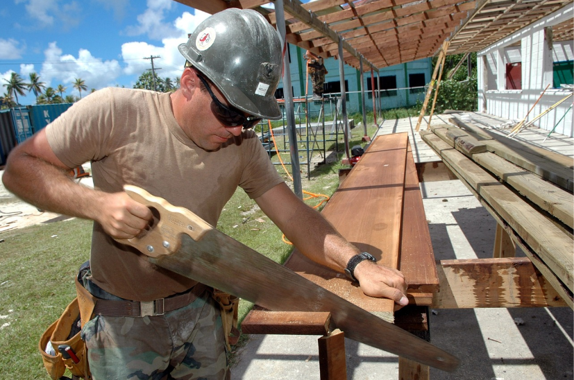 man with hardhat sawing wood outdoors