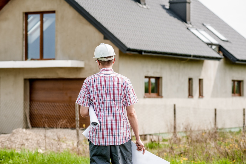 man wearing hardhat with plans looking at house