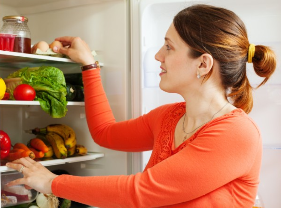 woman wearing orange in front of fridge with fruits and veggies