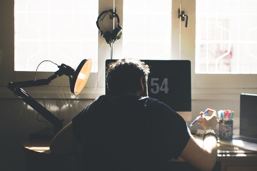 man on desk holding pen with mac screen lamp headset window